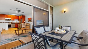 A dining area with a table and chairs, a kitchen in the background, and a sliding glass door leading to an outdoor space. - Upgraded beachside condo with ground floor access (Lahaina)