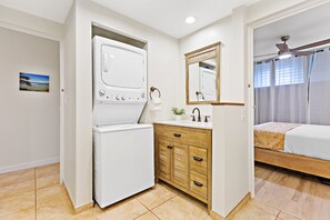 Une chambre d’hôtel équipée d’un lave-linge, de meubles en bois, d’un lit et d’une salle de bain avec un miroir et un lavabo.