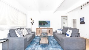 Una sala de estar moderna con dos sofás grises, una mesa de centro y un televisor que muestra una vista panorámica.