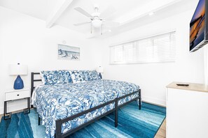 Un dormitorio con cama, escritorio, silla, ventilador de techo, ventana con persianas y televisor de pared.