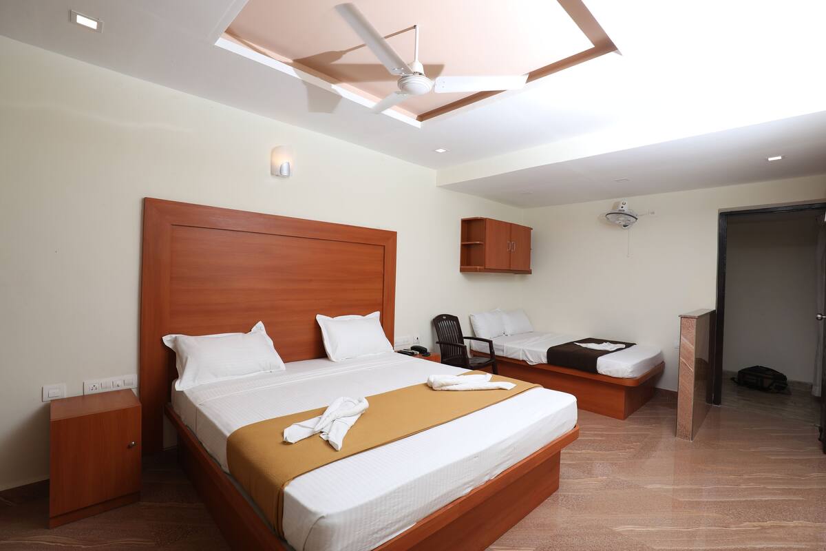 A hotel room with a large bed, a smaller bed, a desk, and a ceiling fan.
