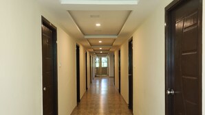 A long, narrow hallway with dark wooden doors on both sides, leading to a bright room at the end. - Hotel Rydham (Madurai)
