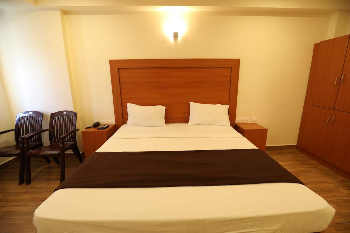 A neatly arranged hotel room with a large bed, wooden headboard, two bedside tables, a nightstand, a wardrobe, and two chairs.