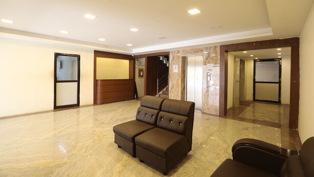 A spacious lobby with a brown sectional sofa, a wooden reception desk, and a marble floor. - Hotel Rydham (Madurai)