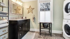 Une buanderie équipée d’un lave-linge, d’un évier, d’un miroir décoré de motifs en forme d’étoiles et d’une fenêtre.