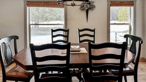 En matplats med ett träbord och stolar, en kristallkrona och två fönster med persienner.