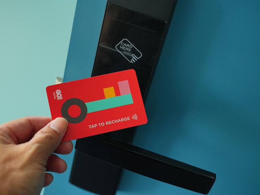 Een hand houdt een rode kaart vast met een symbool voor opladen, voor een blauwe deur met een kaartlezer.