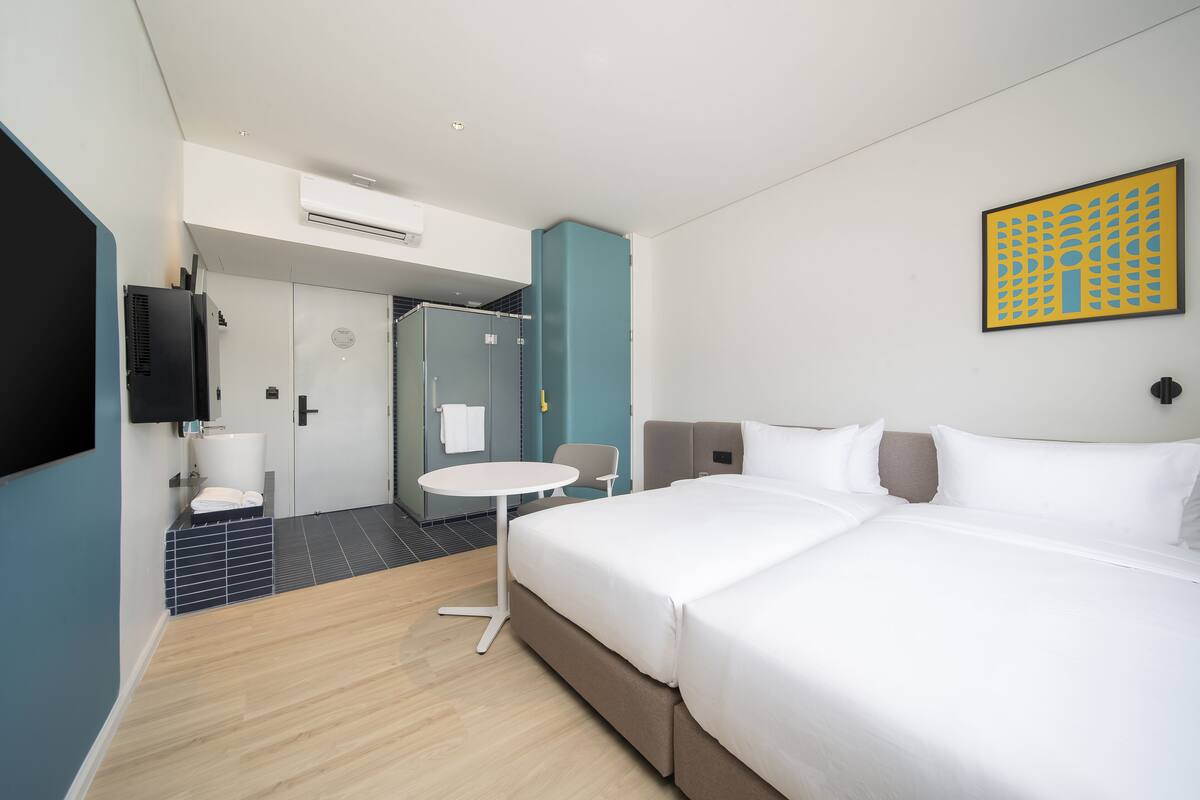 A modern hotel room with a large bed, a small round table, a shower area, and a mounted TV.