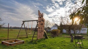 Een houten schommel en een glijbaan in een gazon, met een huis op de achtergrond.