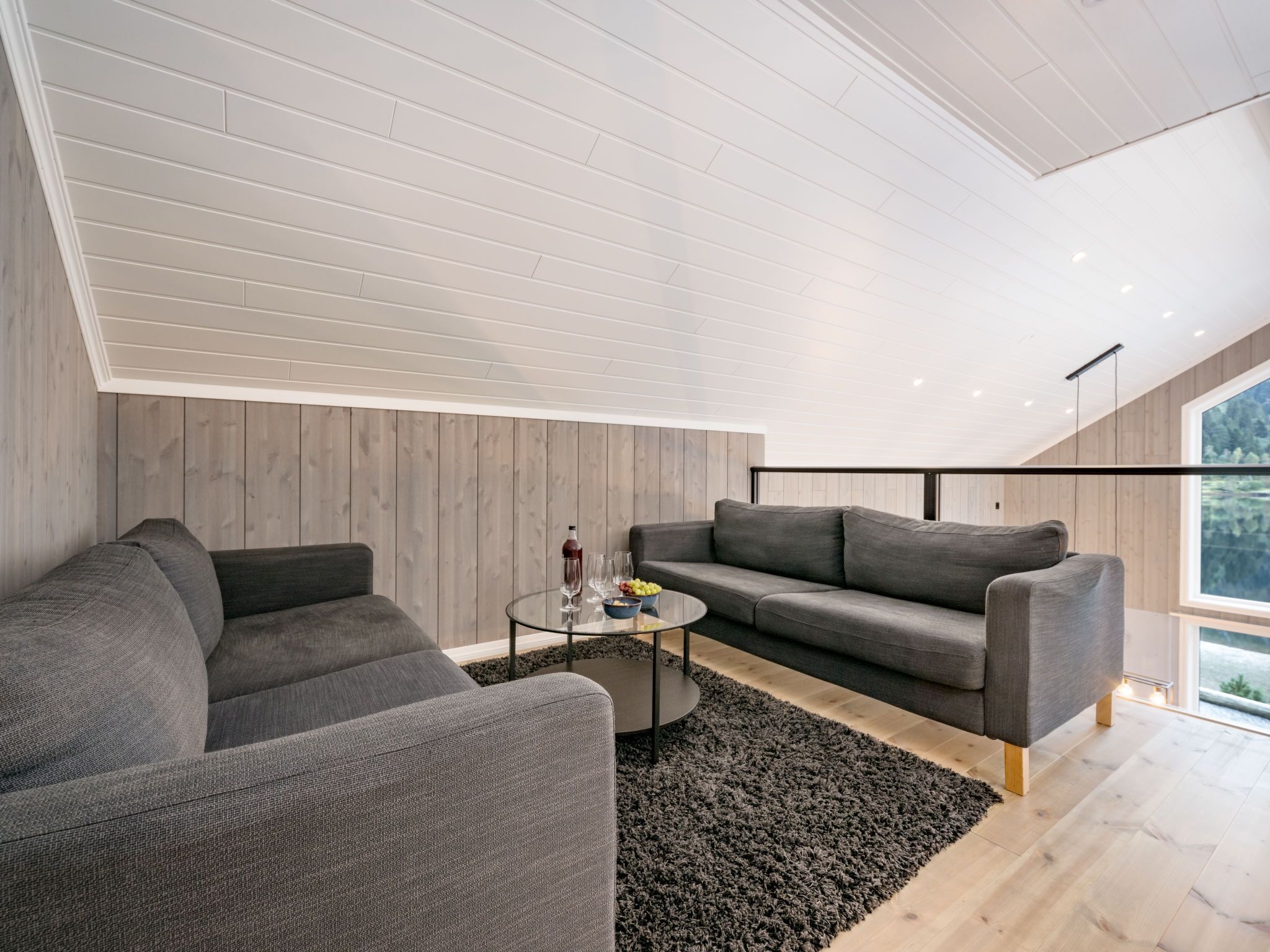 Un salon moderne avec un canapé d’angle gris, une table basse en verre et un tapis noir.