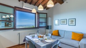 Un área de comedor con una mesa preparada para dos personas, un sofá con un cojín y una ventana con vistas al paisaje.