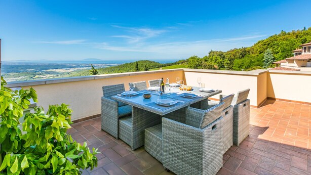 Un espacio de comedor al aire libre con mobiliario de mimbre y una mesa lista para cuatro, con vistas a un paisaje pintoresco.