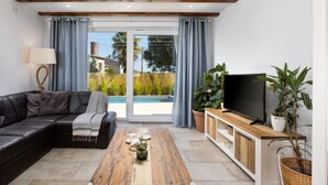 Una sala de estar moderna con un sofá modular, una mesa de centro de madera, un televisor sobre un mueble de madera y una puerta corrediza de vidrio que da a una piscina.