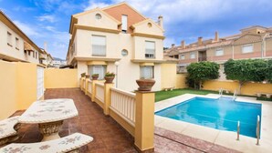 Ein zweistöckiges Haus mit Swimmingpool, einer überdachten Terrasse mit Tisch und Stühlen sowie einem gepflegten Garten.