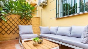 Eine Terrasse mit einer Couch, Kissen, einem Holztisch und einer Pflanze.