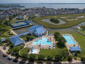 An aerial view of a hotel with multiple swimming pools, a tennis court, and a large building with a blue roof.