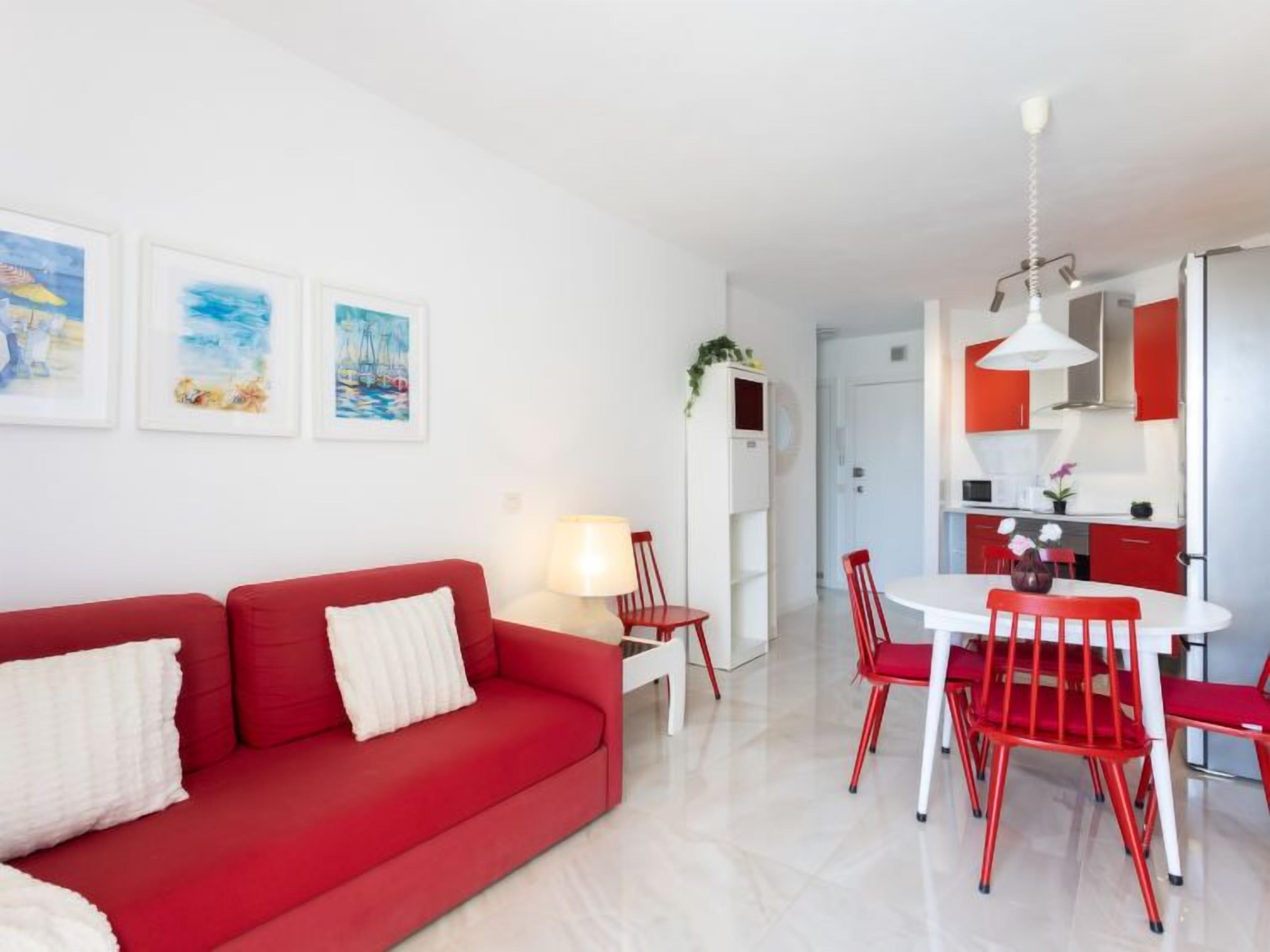A modern living room with a red sofa, a dining table with red chairs, and a kitchen area with red cabinets.