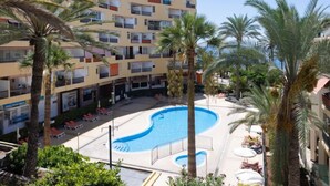 Un hôtel à plusieurs étages doté d’une piscine centrale, entourée de palmiers et de chaises longues.