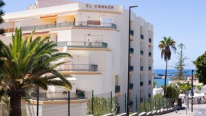 Un hôtel à plusieurs étages, nommé « EL CARMEN », doté de balcons, d’une piscine et offrant une vue sur la mer.