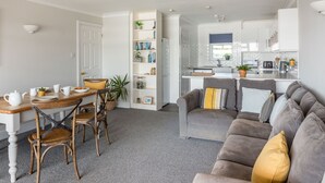 Ein modernes Wohnzimmer mit grauem Sofa, einem Esstisch mit Stühlen und einem Bücherregal.