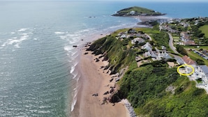 Luftaufnahme einer Küstenstadt mit Strand, Häusern und einem Hügel mit Leuchtturm.