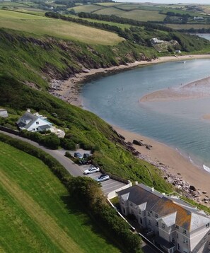 Vue aérienne d’une zone côtière avec un grand bâtiment, une plage et un parking.