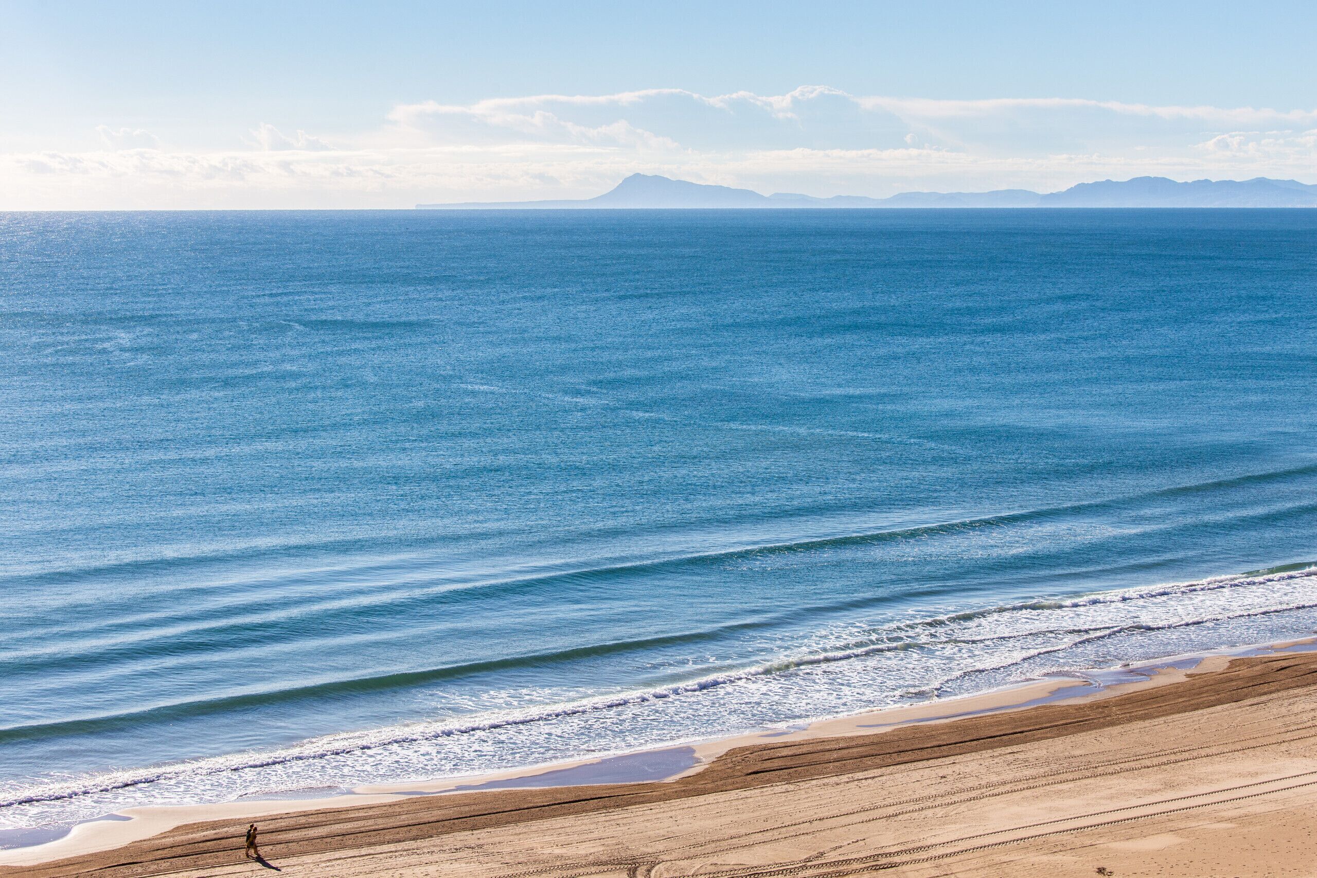 A beach with a clear view of the ocean and distant mountains.