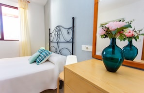 A hotel room with a bed, a wooden dresser, a mirror, and two teal vases with flowers.