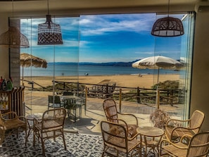 A beachside terrace with wicker furniture, a bar area, and a view of the beach and ocean.
