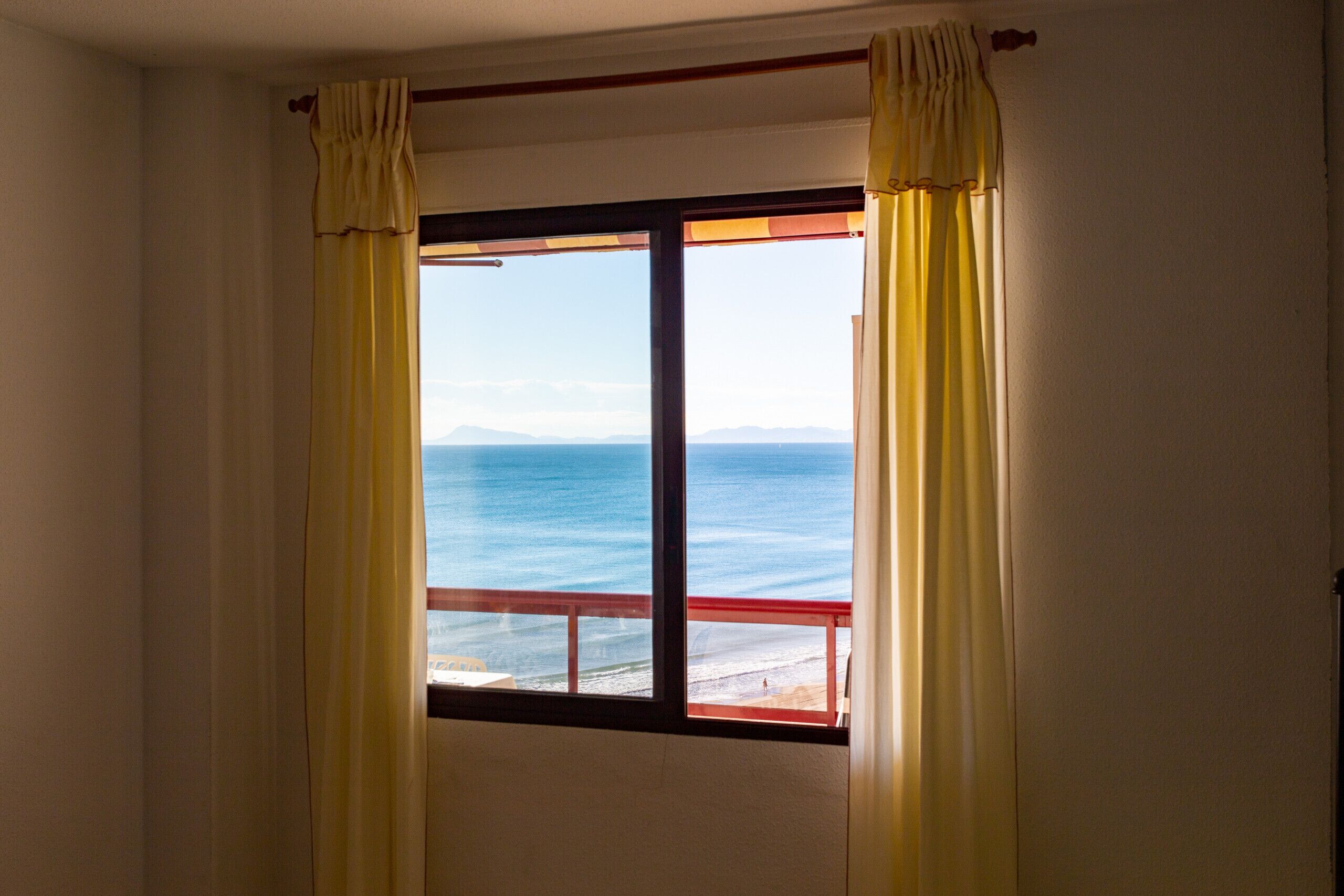 A room with a window overlooking a beach.