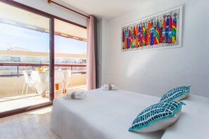 A hotel room with a balcony, a bed with white linens, and a colorful abstract painting on the wall.