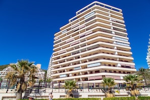 A multi-story hotel with balconies, palm trees, and a clear blue sky.