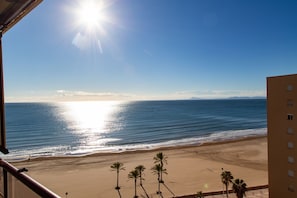 A beach view from a balcony with palm trees and a clear sky.