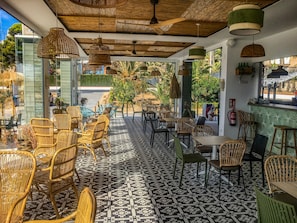 An outdoor seating area with wicker chairs and tables, patterned floor tiles, and hanging wicker lamps.