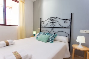 A neatly made bed with white linens and teal patterned pillows, a metal headboard, and a bedside table with a lamp.