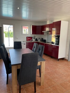 Une cuisine moderne avec des meubles de rangement rouges, une table à manger avec des chaises et une vue sur l’extérieur.