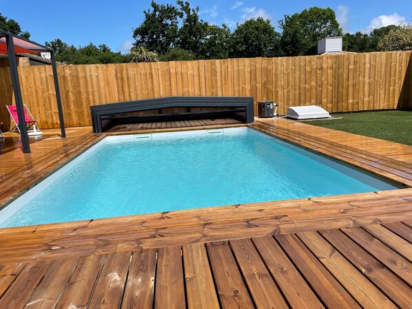 Une piscine rectangulaire entourée d’une terrasse en bois, un jacuzzi et un espace salon abrité.