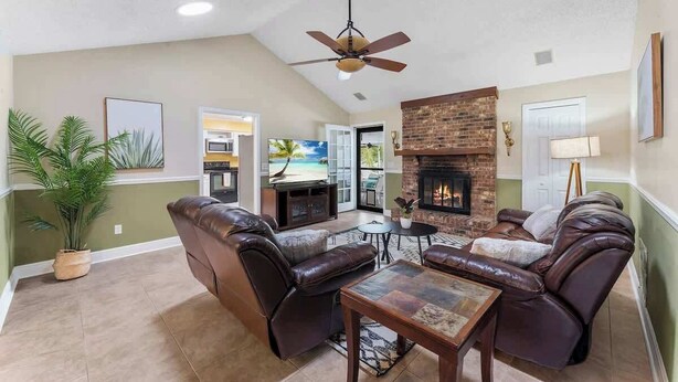 A living room with a fireplace, leather sofas, a ceiling fan, and a view of the outdoors. - Putt Putt Pool Home - Mini Golf,Grill,Ping Pong (Jacksonville)