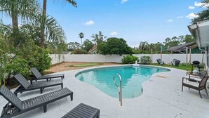 A swimming pool with lounge chairs, surrounded by greenery and a white fence. - Putt Putt Pool Home - Mini Golf,Grill,Ping Pong (Jacksonville)