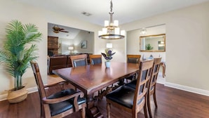 A dining room with a wooden table, chairs, a chandelier, and a potted plant. - Putt Putt Pool Home - Mini Golf,Grill,Ping Pong (Jacksonville)