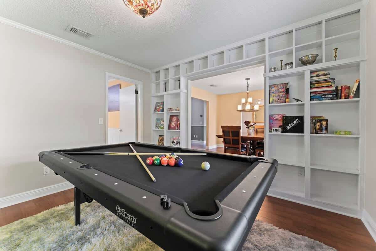 A pool table with balls, a bookshelf, and a dining area.