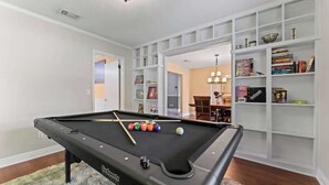 A pool table with balls, a bookshelf, and a dining area. - Putt Putt Pool Home - Mini Golf,Grill,Ping Pong (Jacksonville)