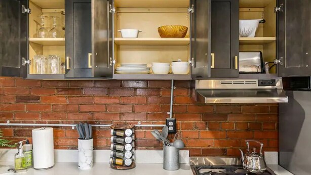 A kitchen with dark cabinets, a brick backsplash, and a stainless steel range hood.