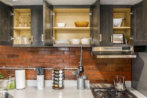 Une cuisine avec des meubles de couleur sombre, un dosseret en briques et une hotte de cuisinière en acier inoxydable.
