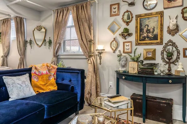 Un salon chaleureux avec un canapé bleu, une table basse et un mur orné de divers tableaux et objets décoratifs encadrés.