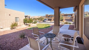 A covered patio with outdoor seating, a small table, and a view of a landscaped area with a lawn and distant buildings. - 4 En Suites on the 18th - Perfect for Golf Groups (Saint George)