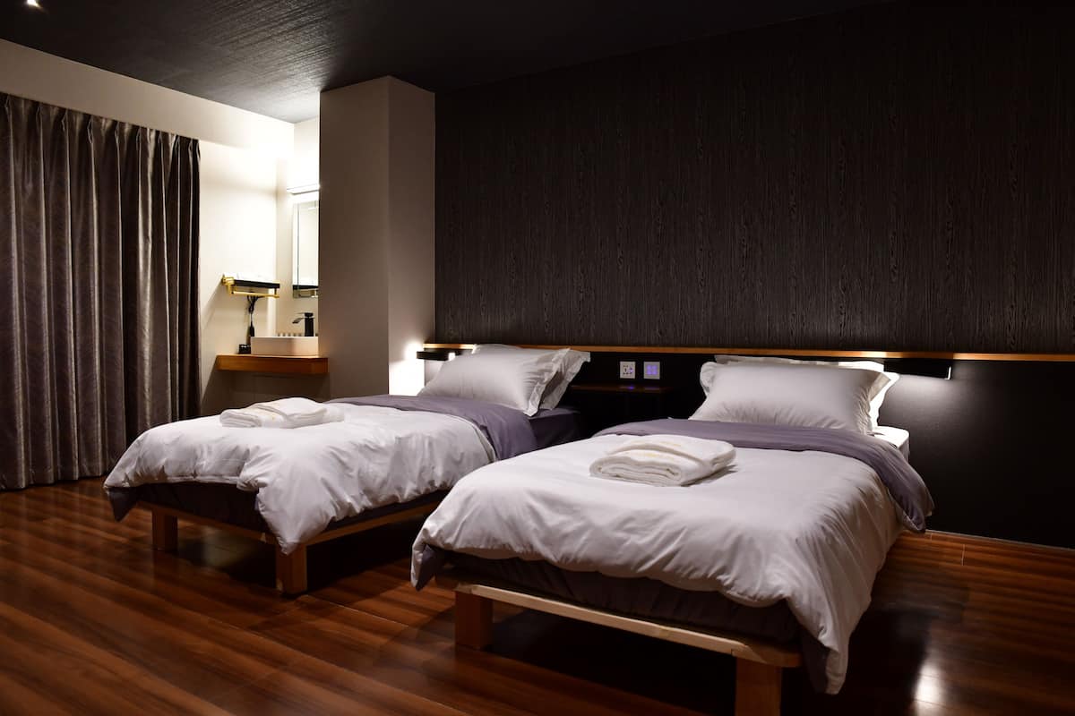 A modern hotel room with two beds, wooden flooring, and a dark accent wall.