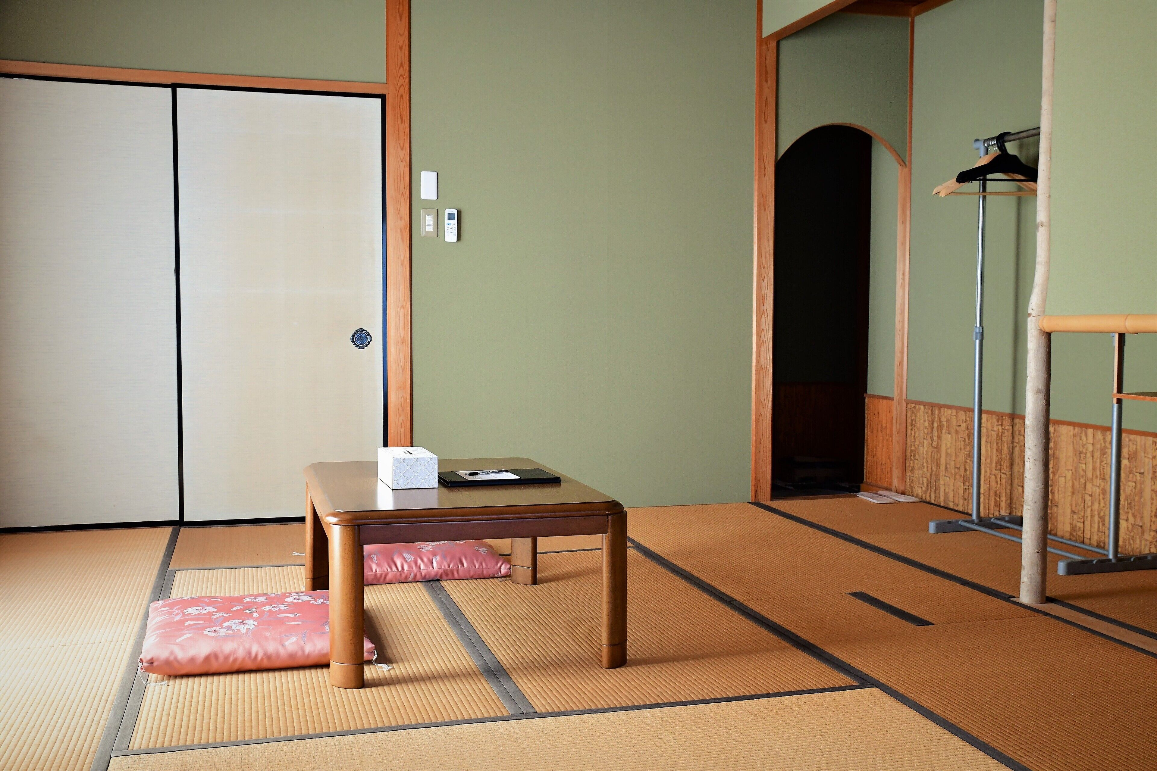 Una habitación japonesa tradicional con suelo de tatami, una mesa de madera baja, un cojín rosa y una puerta corredera.