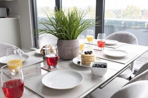 A breakfast table set with plates, glasses, a bowl of blueberries, a plant, and a stack of pancakes. - Elliot Oliver - Stunning 3 Bedroom Penthouse With Large Terrace And Parking (Gloucester)