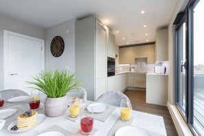A modern kitchen with white cabinets, a dining area with a table set for breakfast, and a large window providing a view of the outdoors.